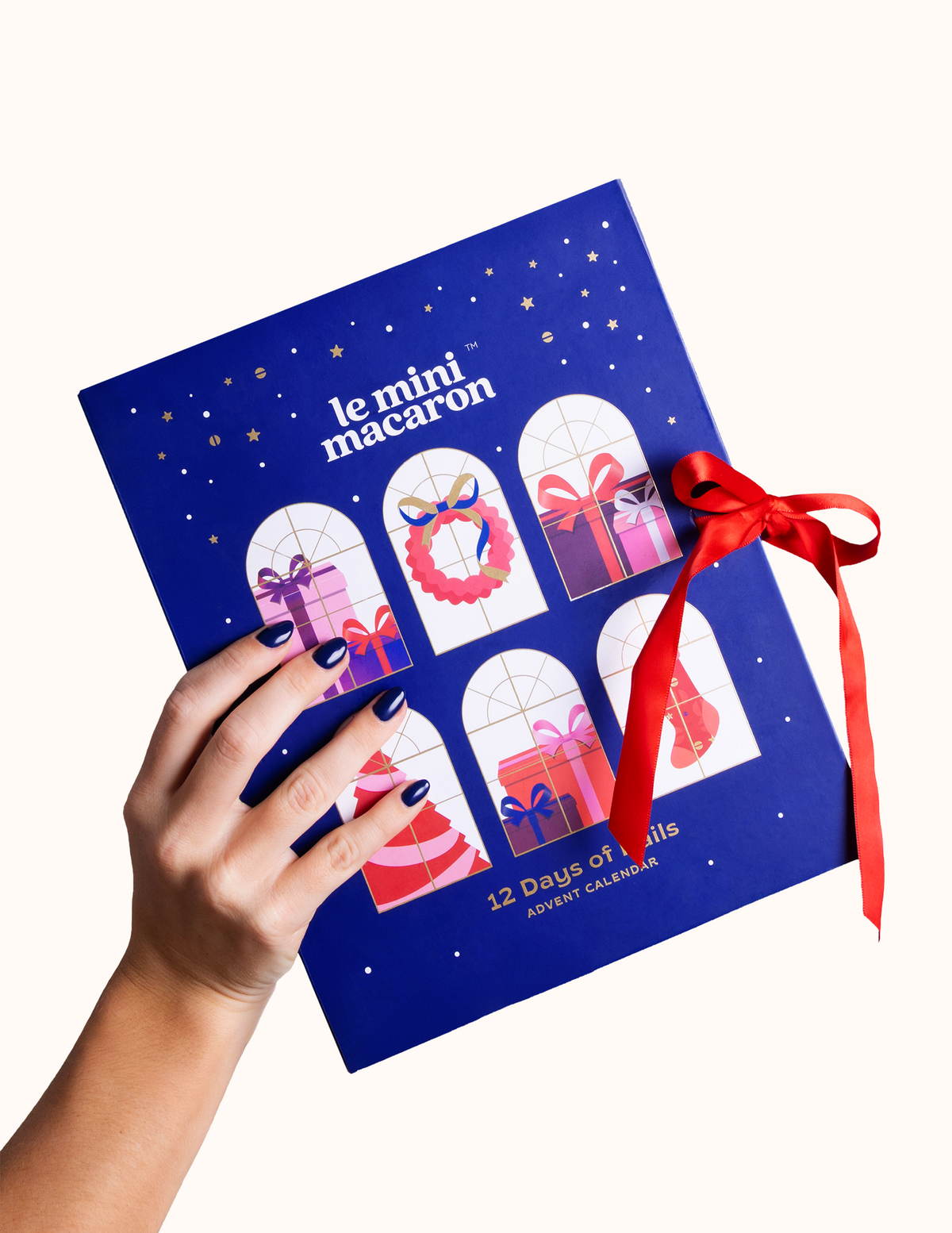 Hand holding 12 Days of Nails Advent Calendar box with a red ribbon in a clean backgorund.