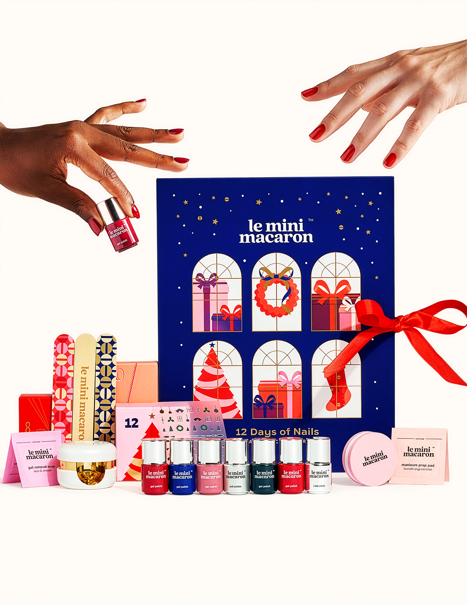 Le Mini Macaron 12 Days of Nails Advent Calendar open display, showing all included products with two hands reaching in to pick them up.